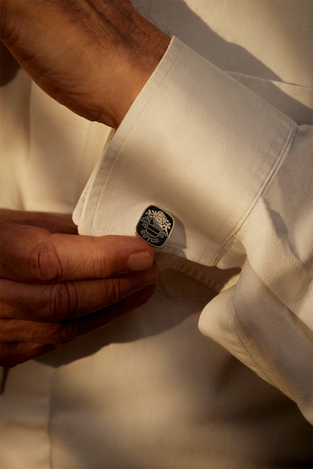 A cufflink with an engraved crest on a white shirt cuff.