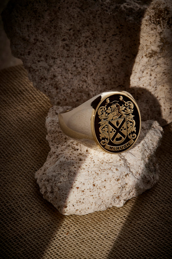 Gold signet ring featuring the McHugh family crest, elegantly displayed on a rugged stone backdrop.