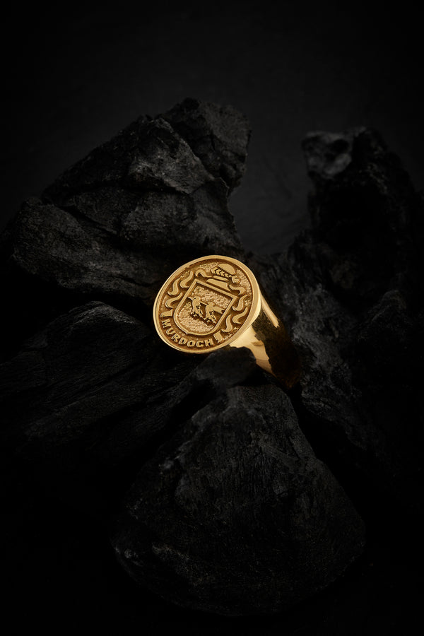 Murdoch family gold signet ring, set against textured dark rock for a bold, timeless presentation.