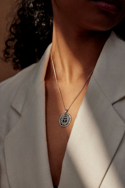 A woman wearing a sterling silver crest pendant necklace on a white blazer.