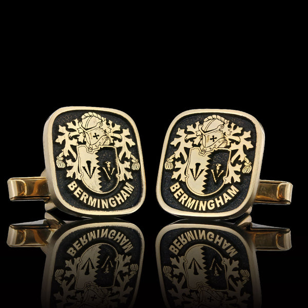 Gold cufflinks with engraved family crest and 'Bermingham' name, reflecting elegantly on a black surface.