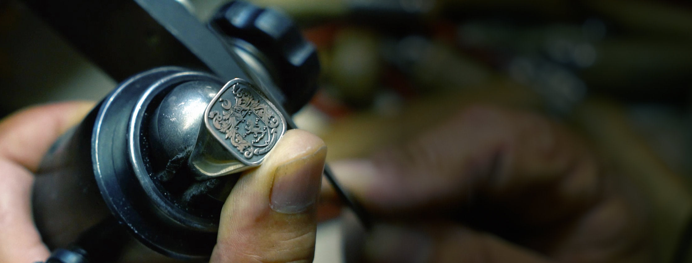 A craftsman engraving intricate details on a silver signet ring.