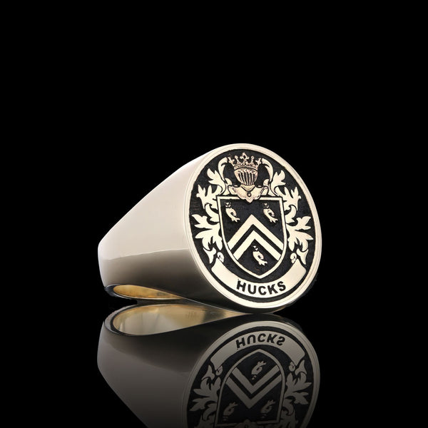 Hucks family gold signet ring, featuring a chevron crest design, displayed on a reflective black surface.