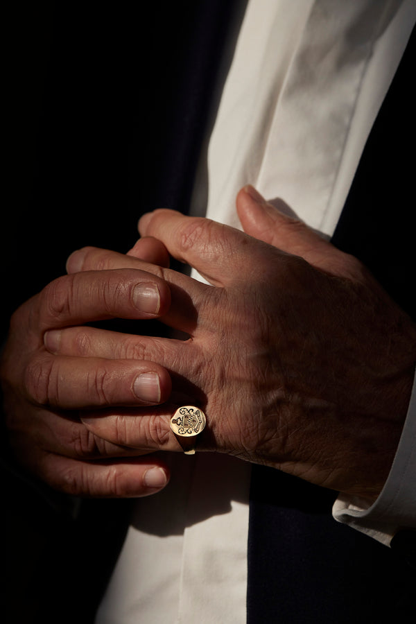 Elegant gold ring with custom family crest worn on the hand of a person in formal attire and soft light.