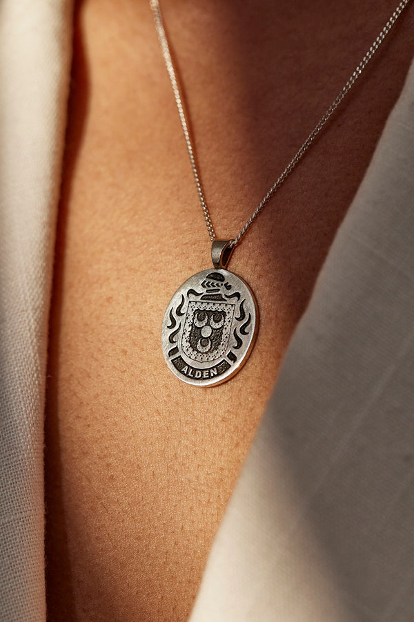 Silver pendant engraved with the Alden coat of arms, elegantly displayed against a warm, natural background.