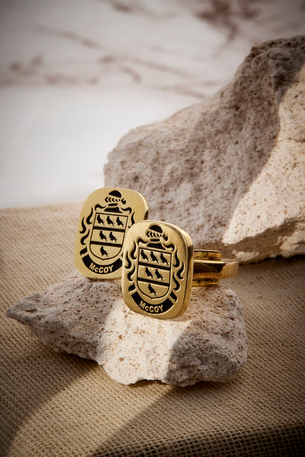 A pair of gold cufflinks with engraved family crests displayed on textured stones.