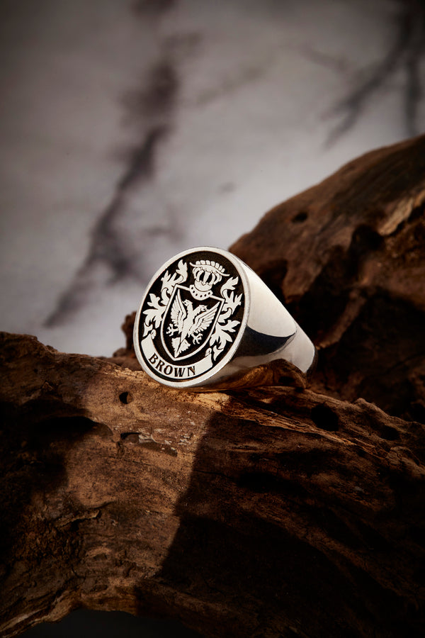 Silver ring engraved with the Brown coat of arms, beautifully set on a textured wooden surface for a rustic look.