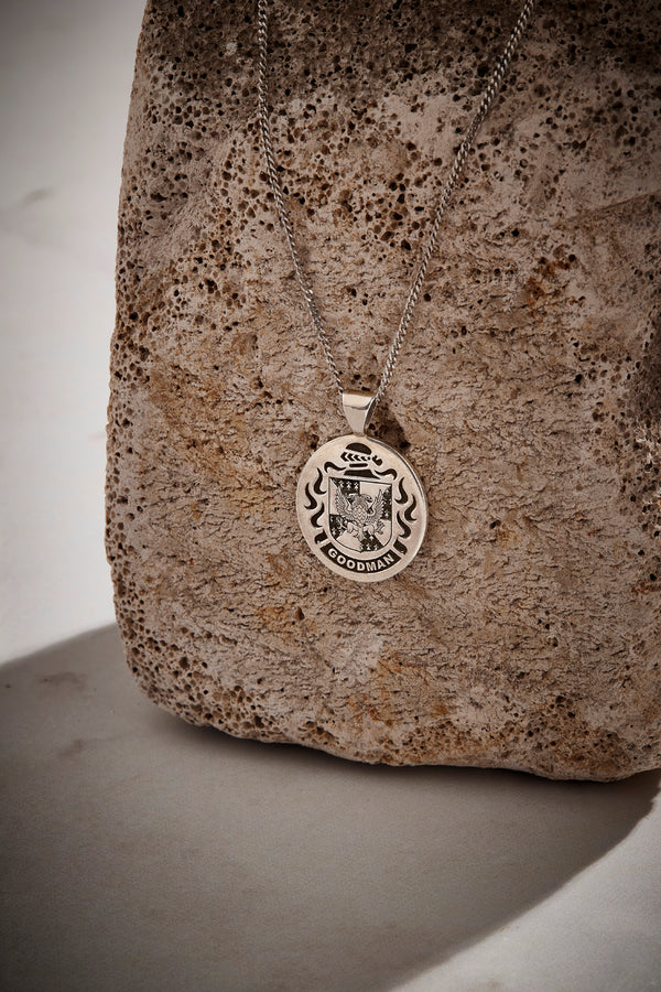 Goodman family crest pendant in silver, showcased against a rugged stone surface, highlighting its timeless appeal.