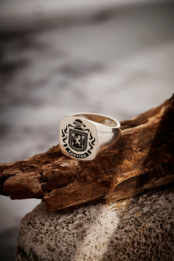 Silver signet ring featuring the Canton crest, placed on natural wood, representing heritage.