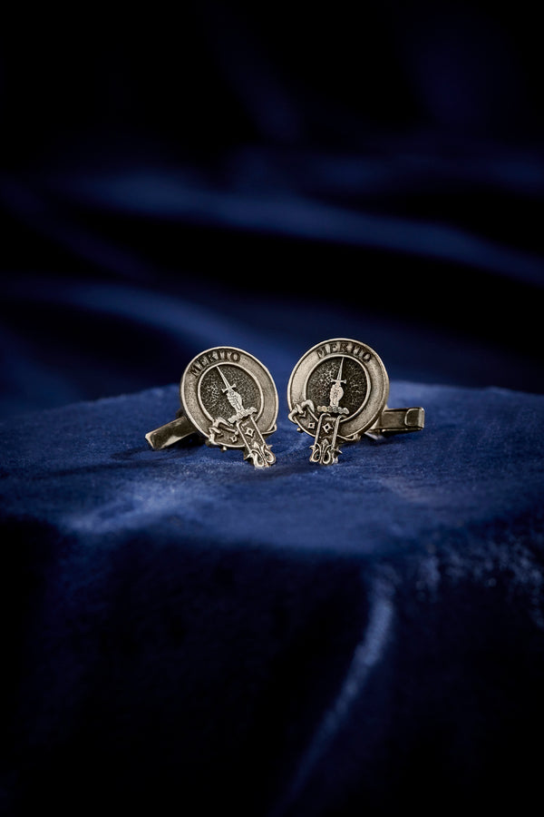 Ornate cufflinks engraved with "Merito" and a detailed sword design, presented on a luxurious dark blue fabric.