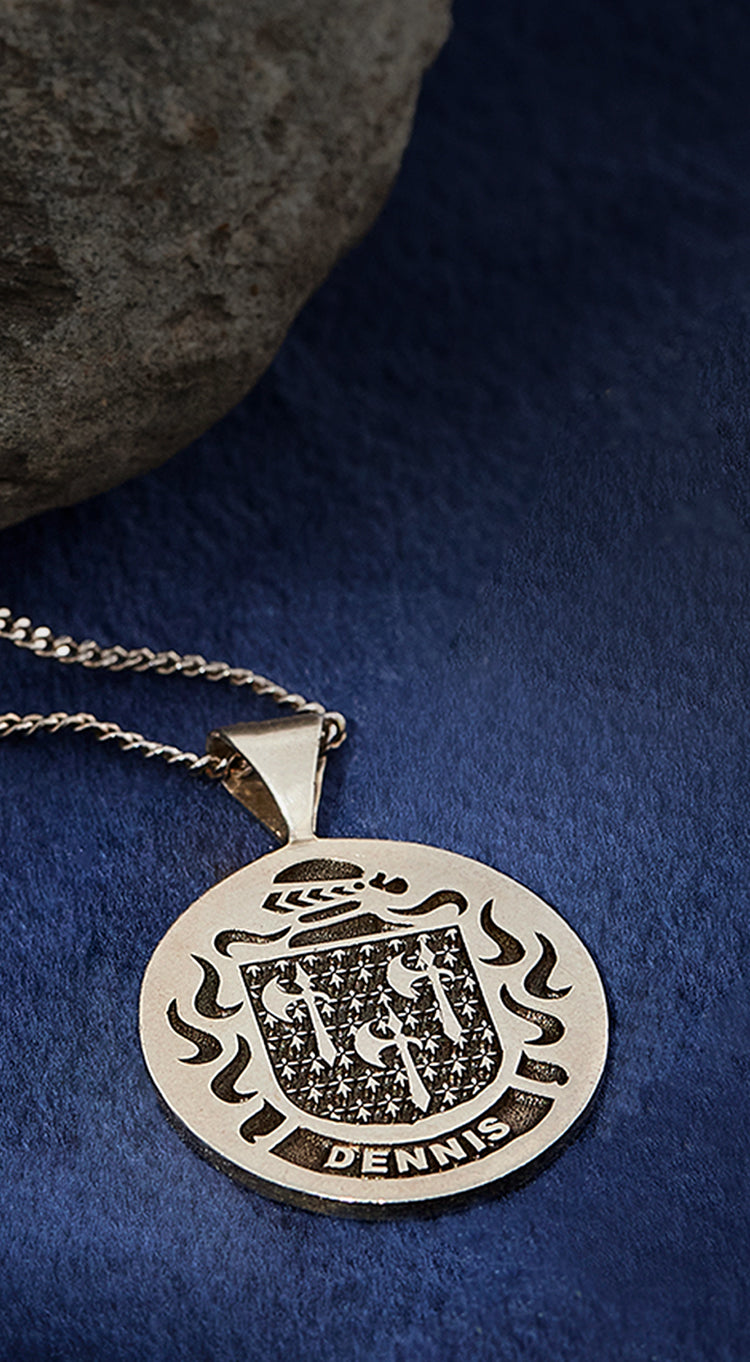 Sterling silver pendant with the Dennis family crest, displayed on a silver chain against a rich blue velvet background.