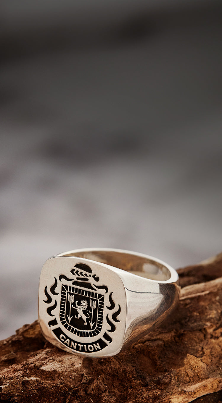 Sterling silver signet ring with the CANTION family crest and name, on rugged wood with a blurred background.