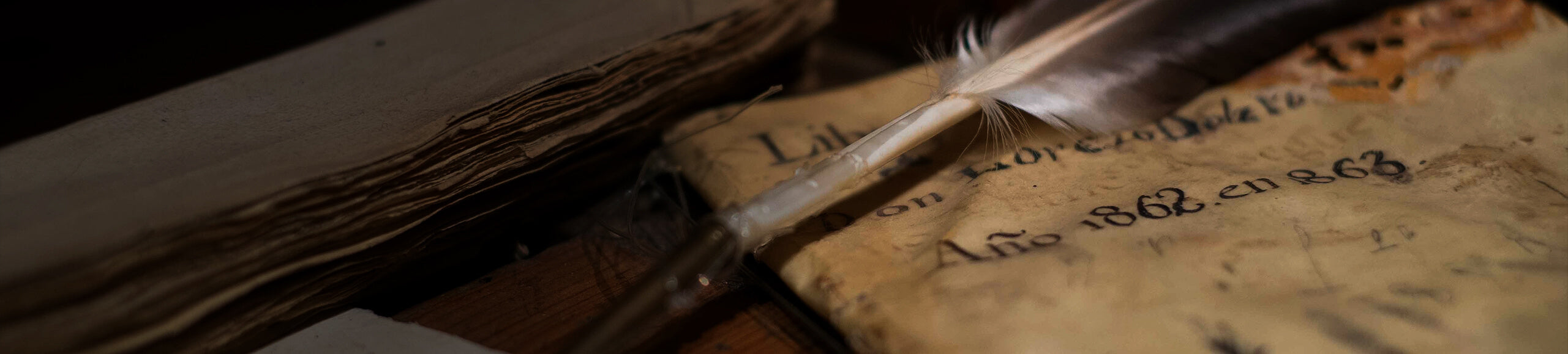 Quill pen resting on an aged parchment with handwritten text, next to stacked antique books.