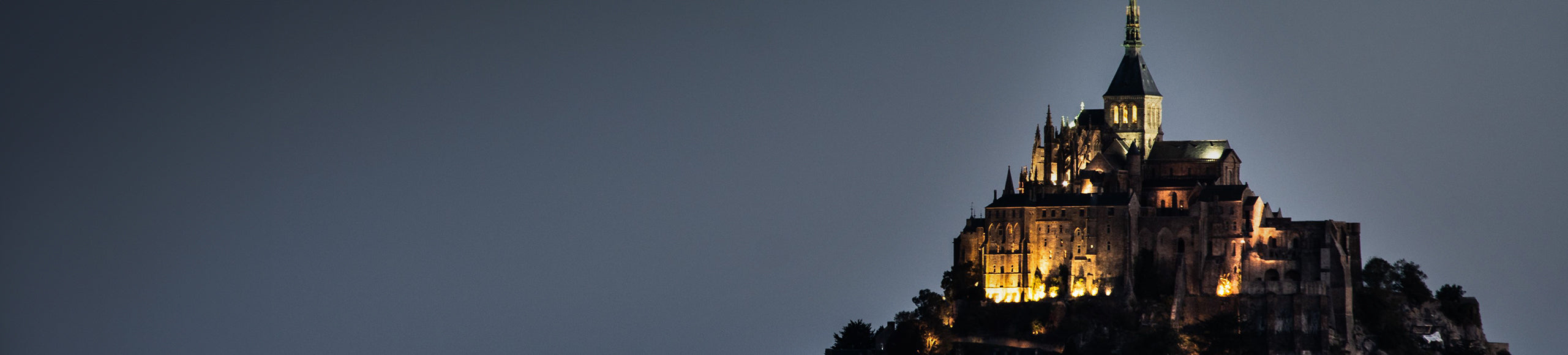 A majestic castle perched on a hilltop at night, illuminated against a dark sky.