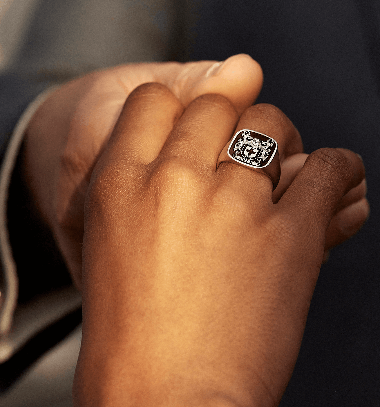 A close-up of two hands, one wearing an engraved sterling silver signet ring.