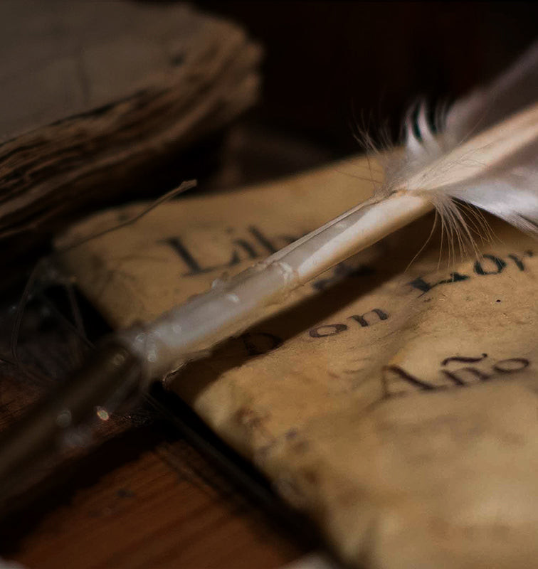 Quill pen resting on an aged parchment with handwritten text, next to stacked antique books.