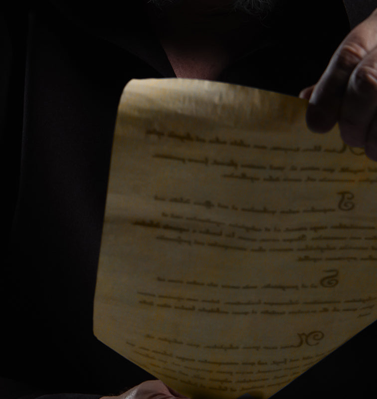 Close-up of a historical document held by a person in dark robes, illuminated under soft lighting.