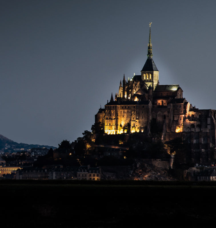 A majestic castle perched on a hilltop at night, illuminated against a dark sky.