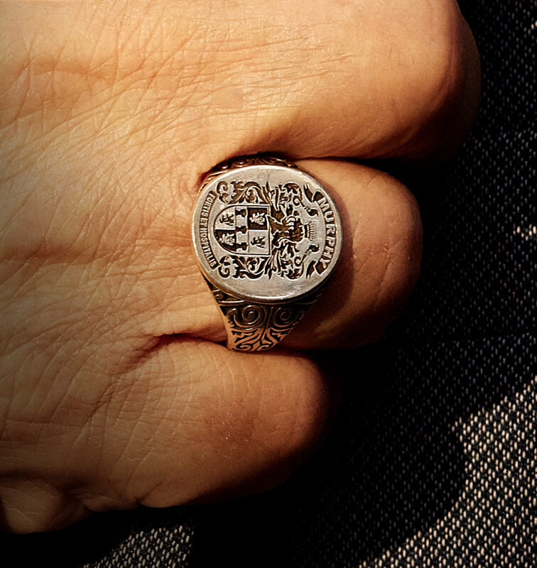 Hand wearing an ornate signet ring, against a tailored suit.