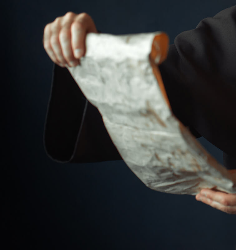 Dark background with a figure holding an unrolled parchment in a scholarly setting.