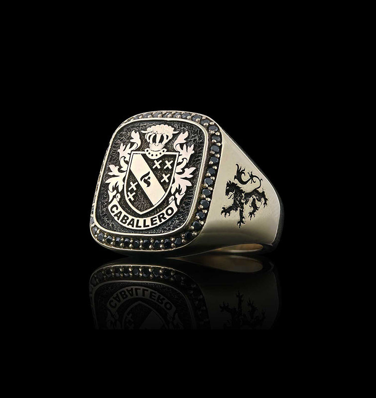 A gold custom signet ring engraved with the name "Caballero," reflected on a glossy black surface.