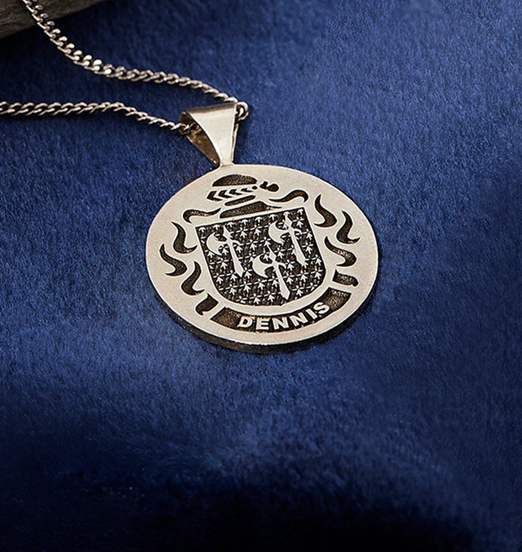 Sterling silver pendant with the Dennis family crest, displayed on a silver chain against a rich blue velvet background.