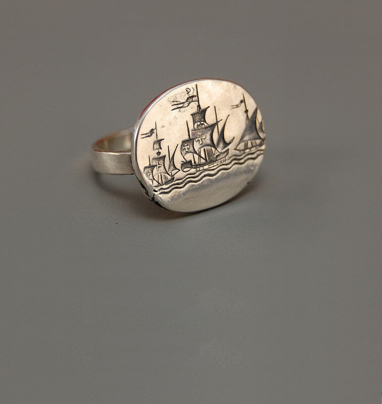 Gray background showcasing a silver ring engraved with a ship design.