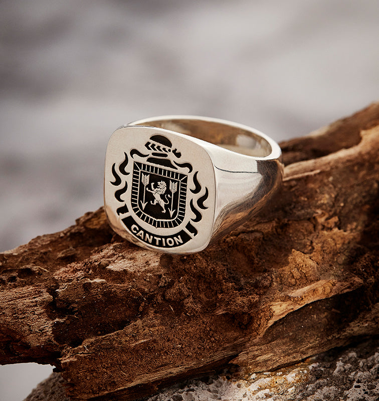 Sterling silver signet ring with the CANTION family crest and name, on rugged wood with a blurred background.