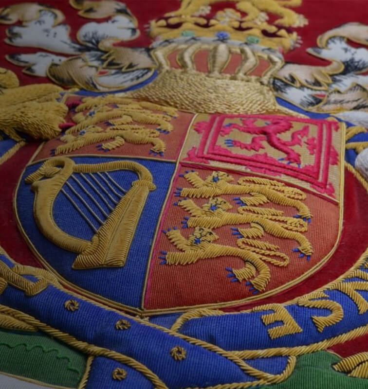 Close-up of an embroidered crest with a harp and lions on red and blue fabric.