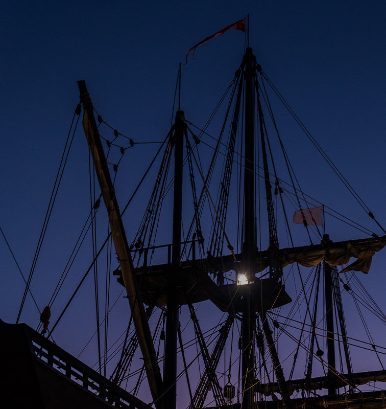 Silhouette of a vintage sailing ship's masts and rigging against a twilight sky.