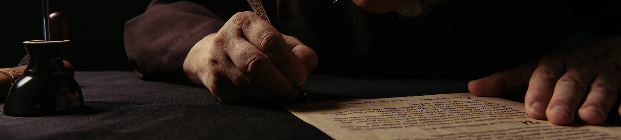 Dark background with a hand writing on parchment using a quill pen.