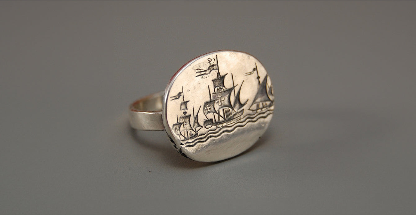 Gray background showcasing a silver ring engraved with a ship design.