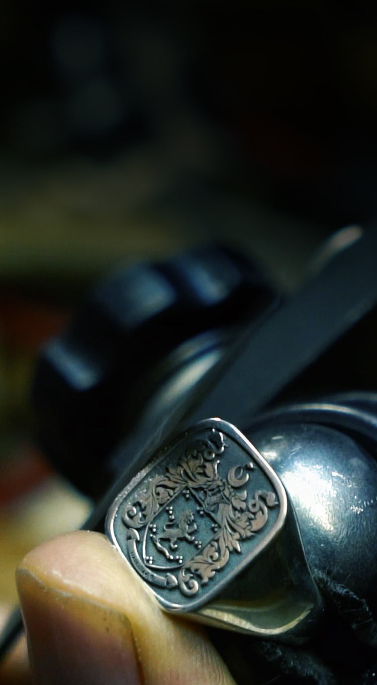 A craftsman engraving intricate details on a silver signet ring.