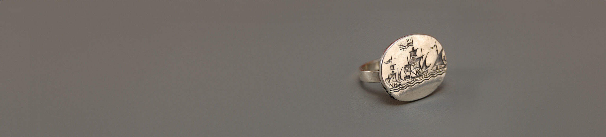 Gray background showcasing a silver ring engraved with a ship design.