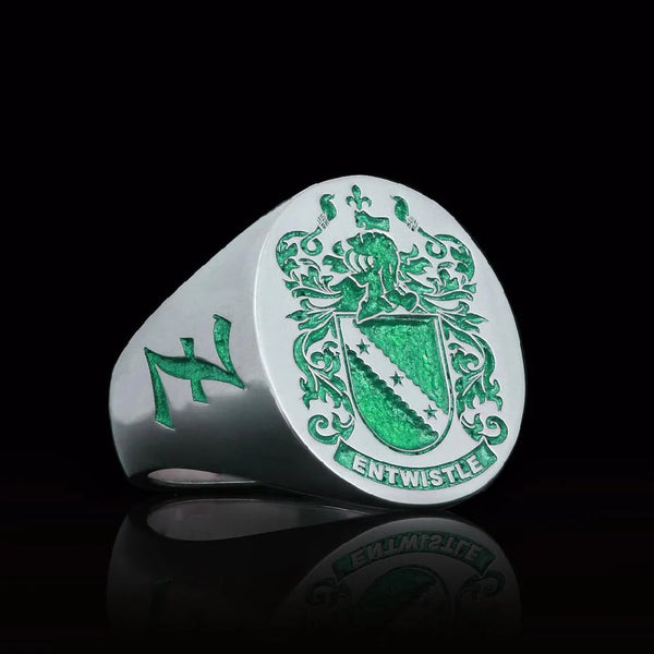 Silver ring engraved with green family crest and name 'Entwistle,' highlighted on a reflective black background.